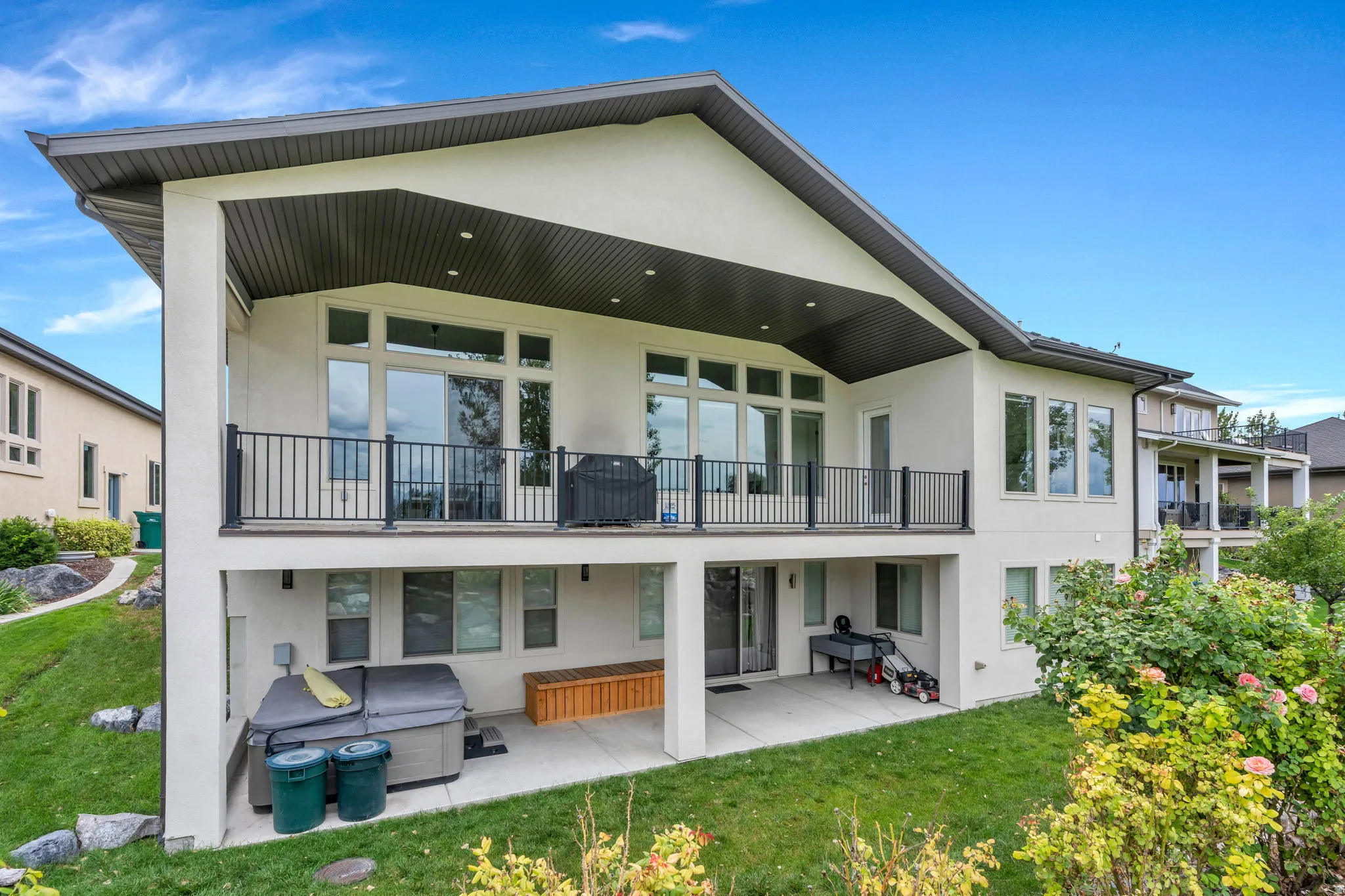 Multi-level stucco exterior with an upper covered balcony featuring black railings, and a lower covered patio