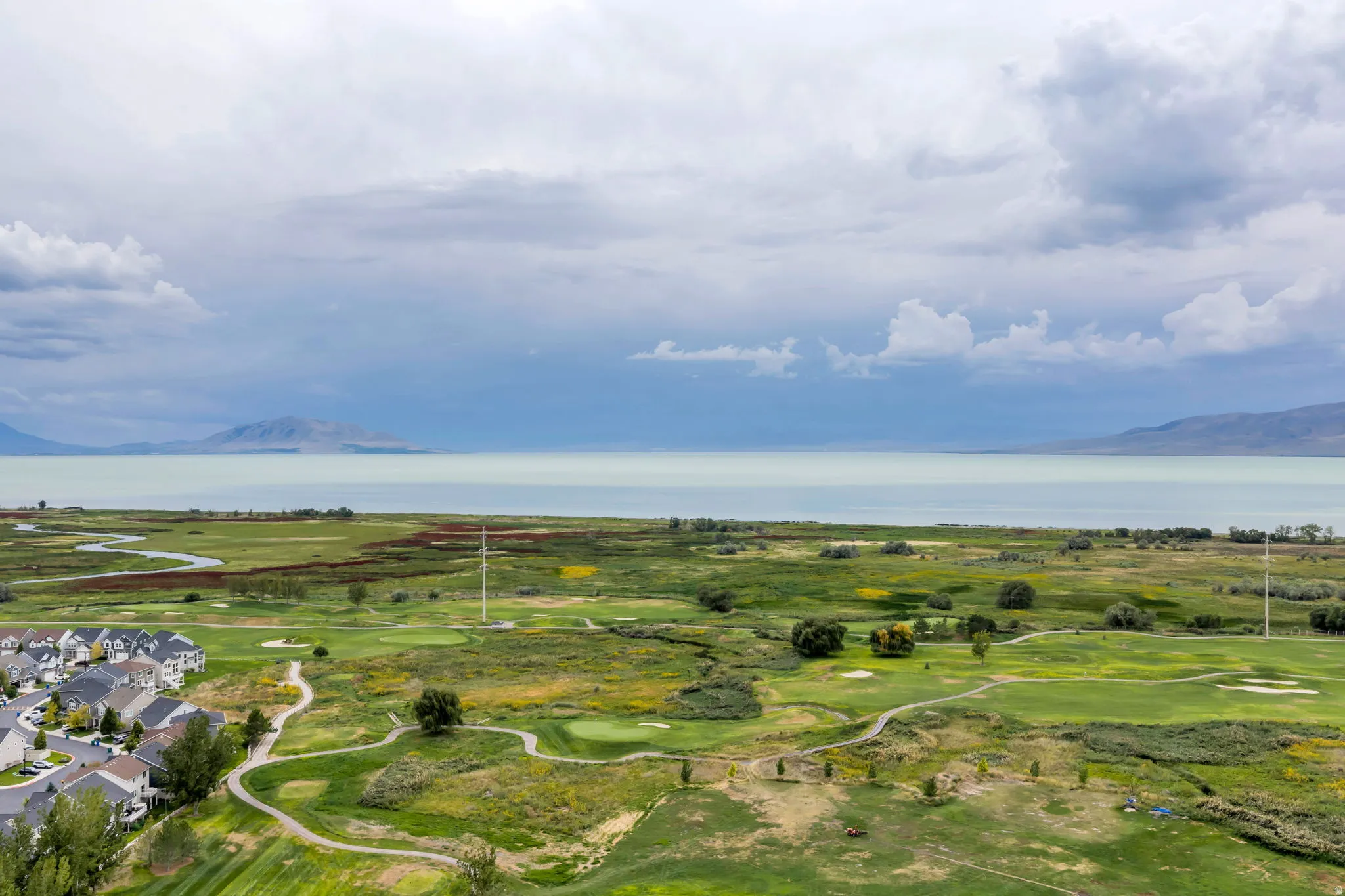 Expansive golf course frontage with winding cart paths, bordering a tranquil lake with distant mountains