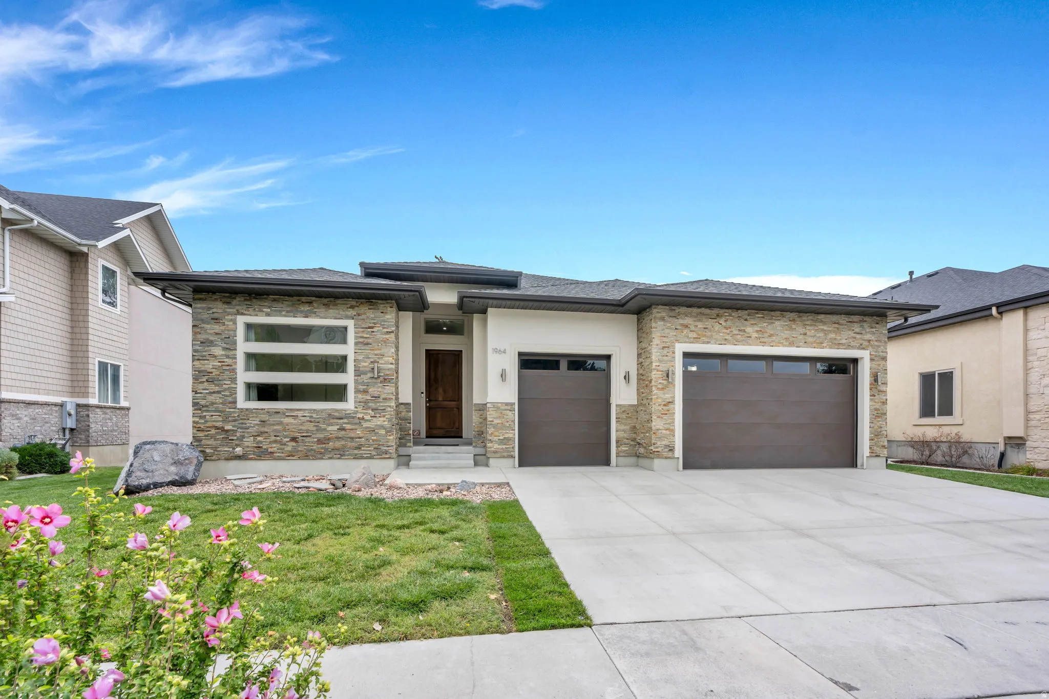 Contemporary single-story residence featuring a stone and stucco exterior, dark wood-finish entry door, and a two-car garage with dark paneled doors