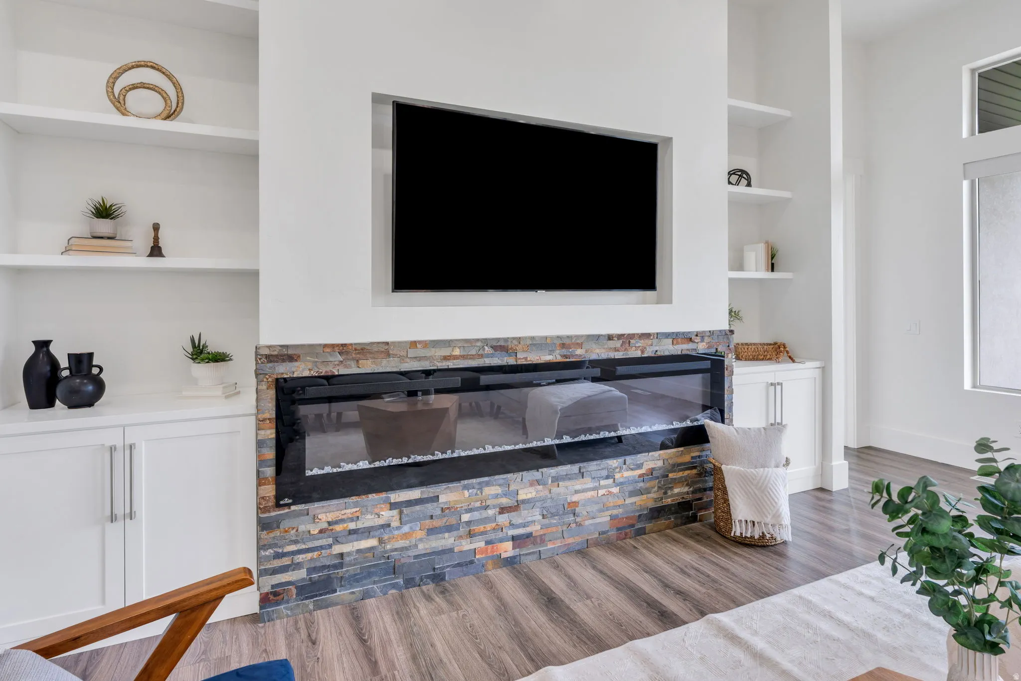 Built-in shelving, stone-surround linear fireplace, integrated television niche, wood-finish flooring, and white cabinetry
