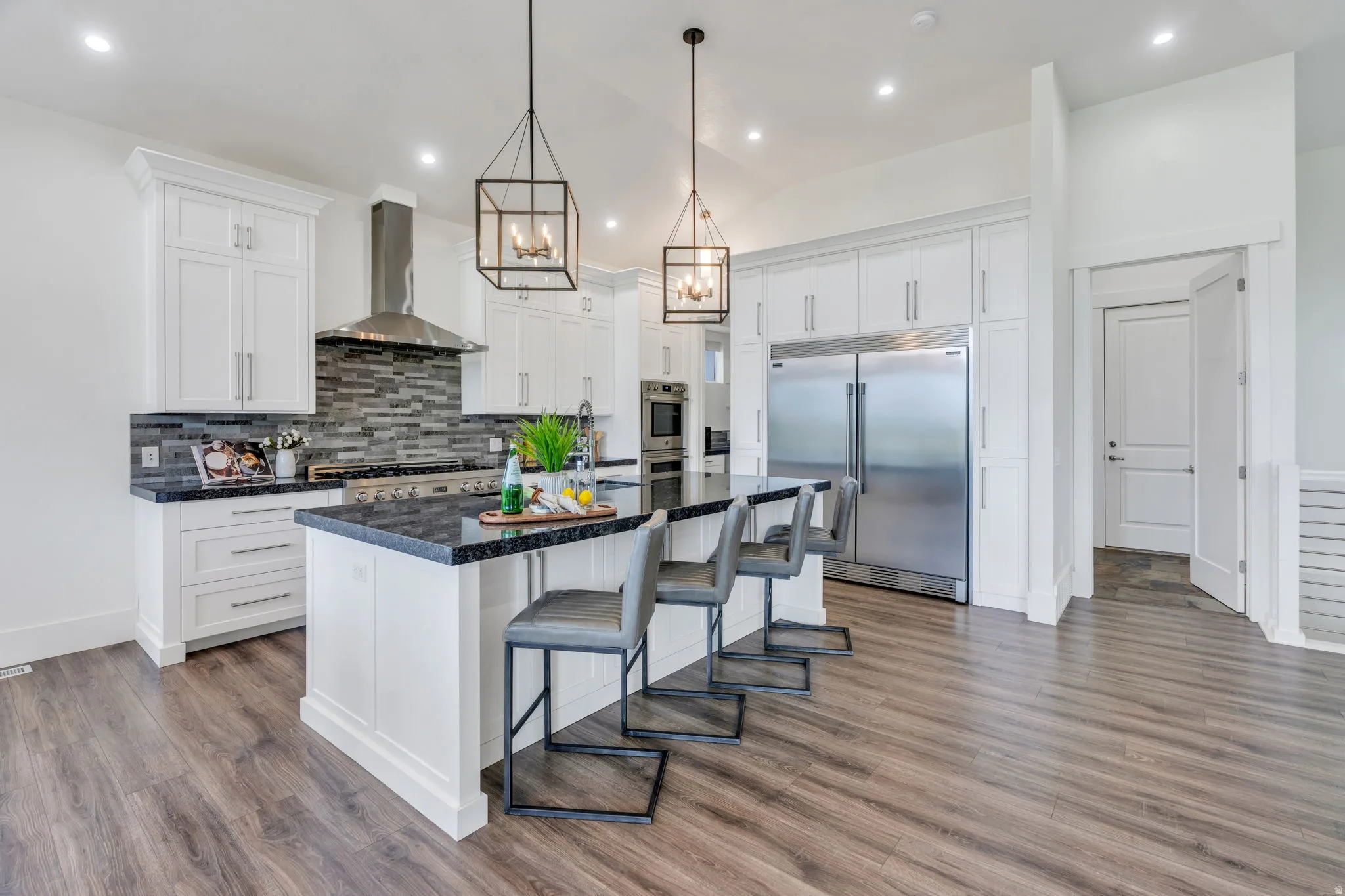 Expansive kitchen featuring white cabinetry, dark stone countertops, wood-finish flooring, stainless steel appliances, and pendant lighting