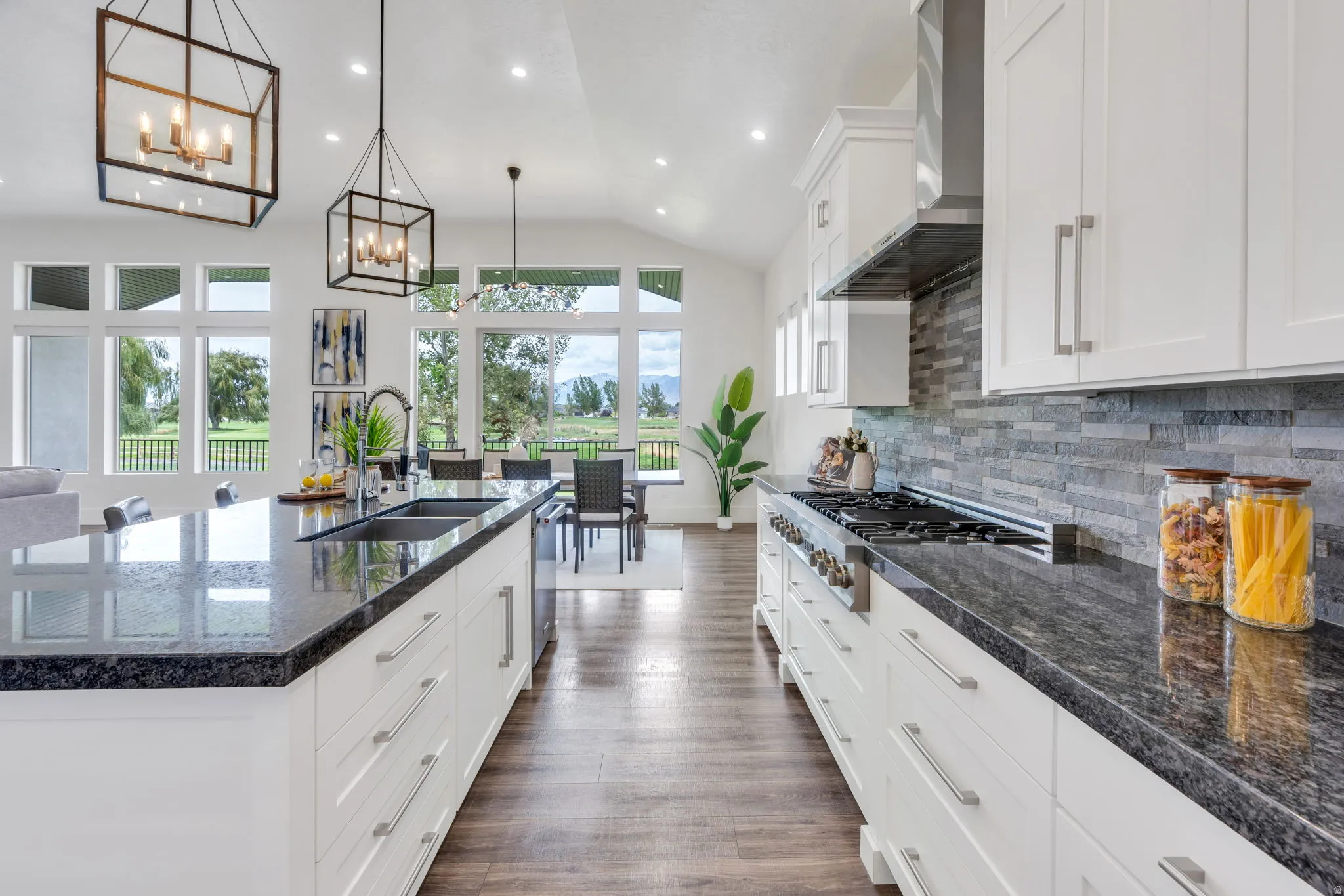 Kitchen featuring an expansive island with an undermount sink, dark stone countertops, white cabinetry with silver-tone pulls, and a stone-tile backsplash