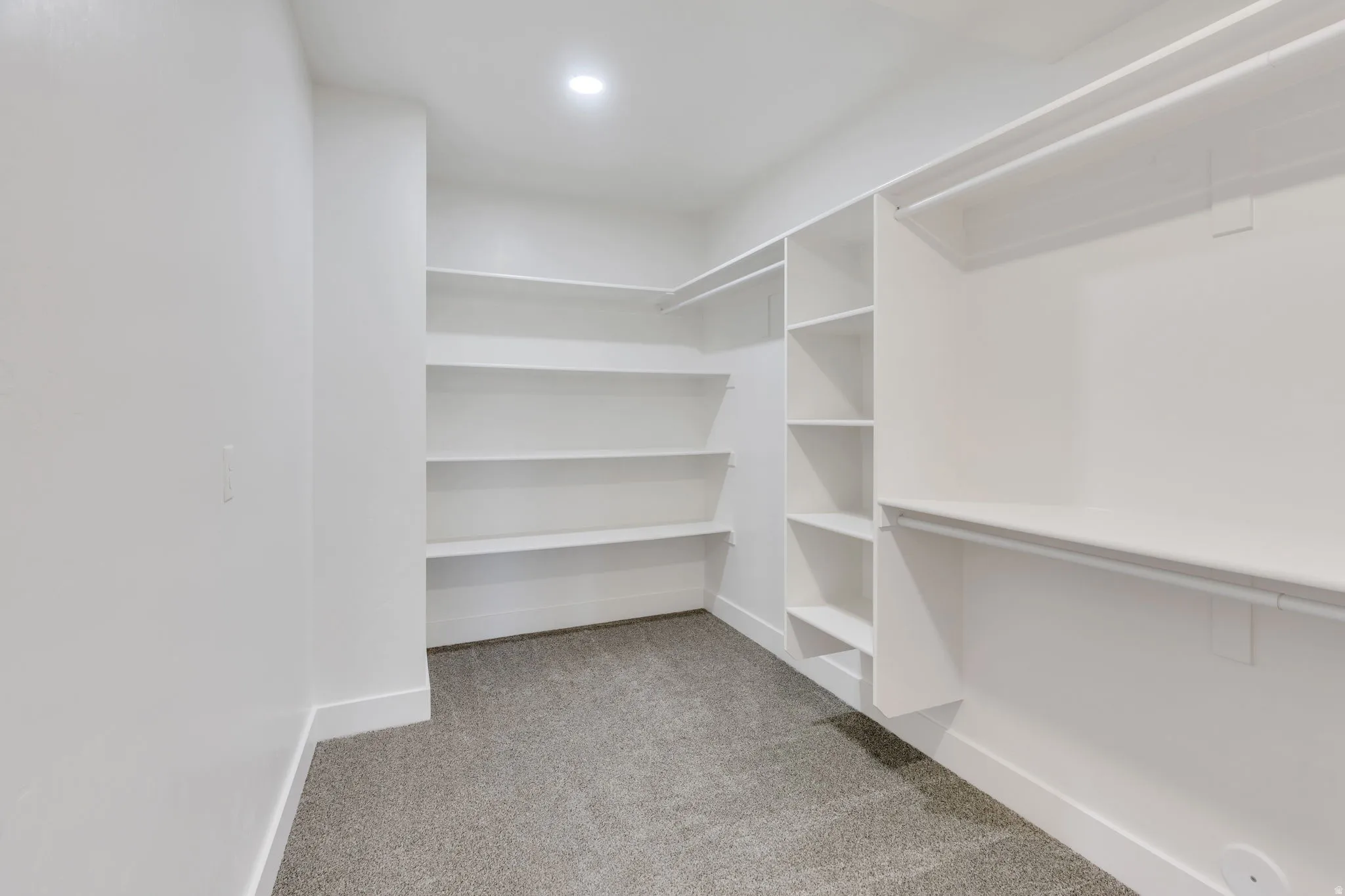 Recessed lighting illuminates extensive built-in shelving, hanging rods, and gray carpet