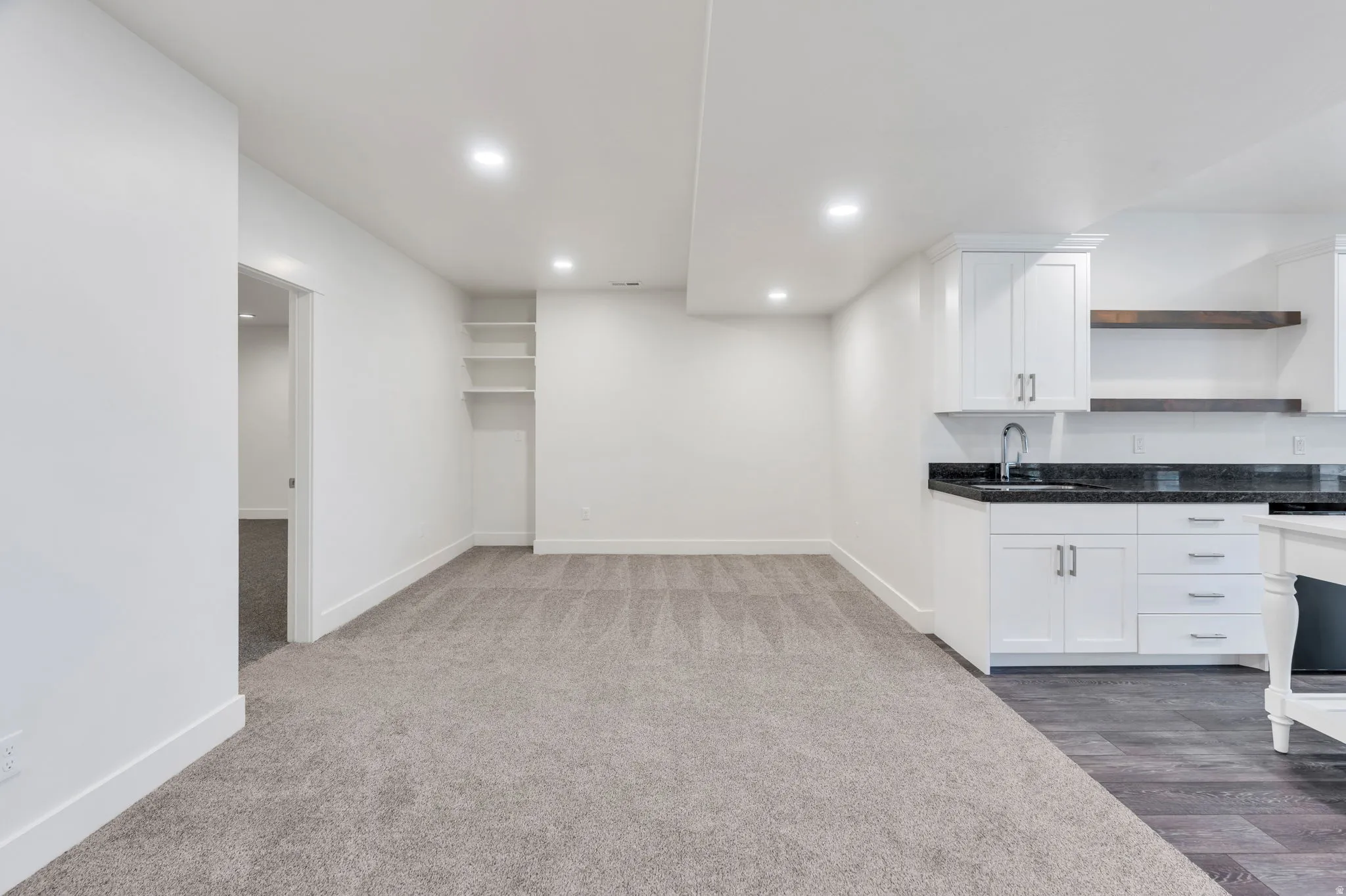 Recessed lighting, built-in shelving, white cabinetry, dark stone countertop, and wood-finish flooring