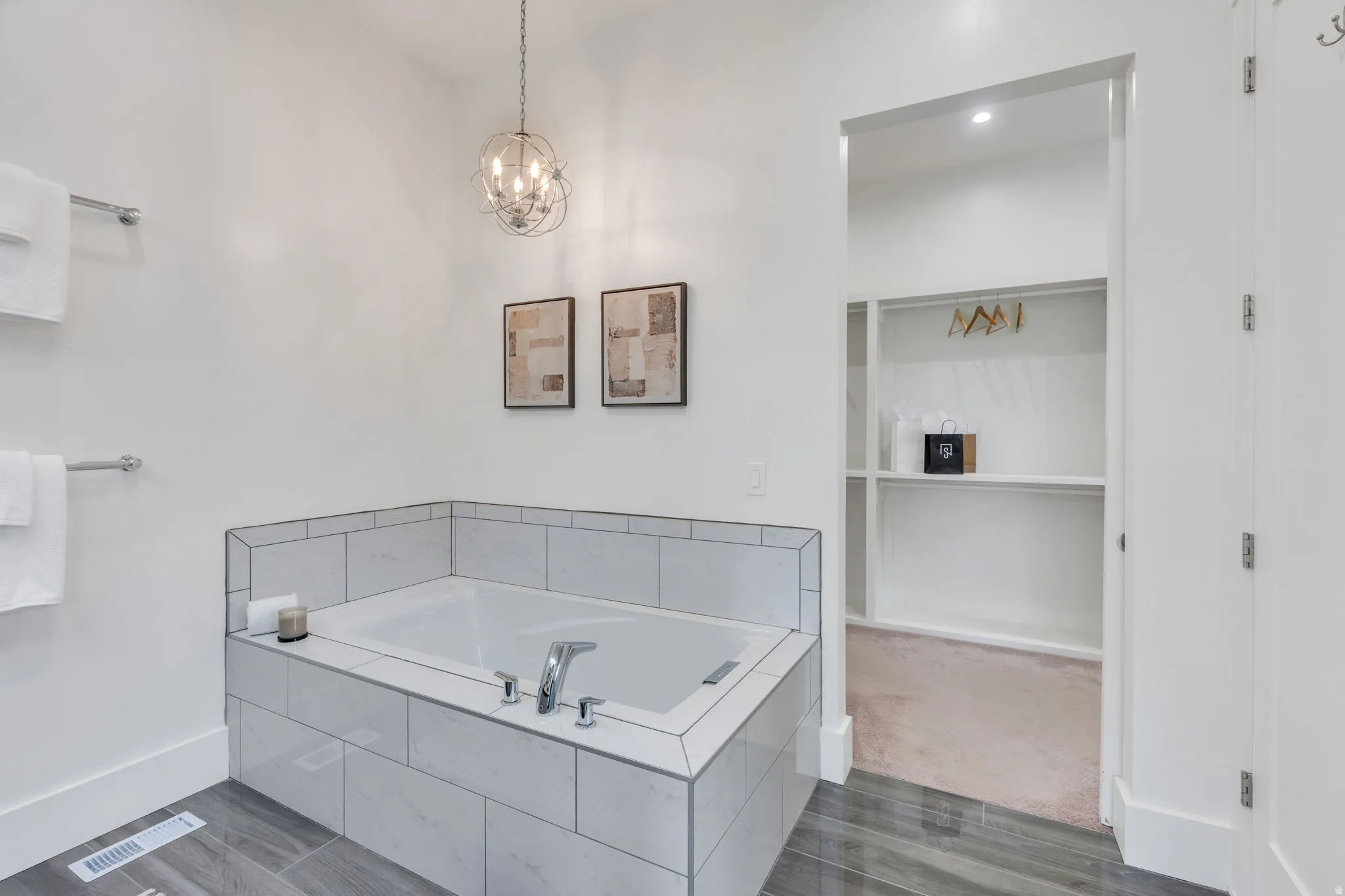 Soaking tub with tile surround, wood-finish flooring, recessed lighting, and an adjacent walk-in closet