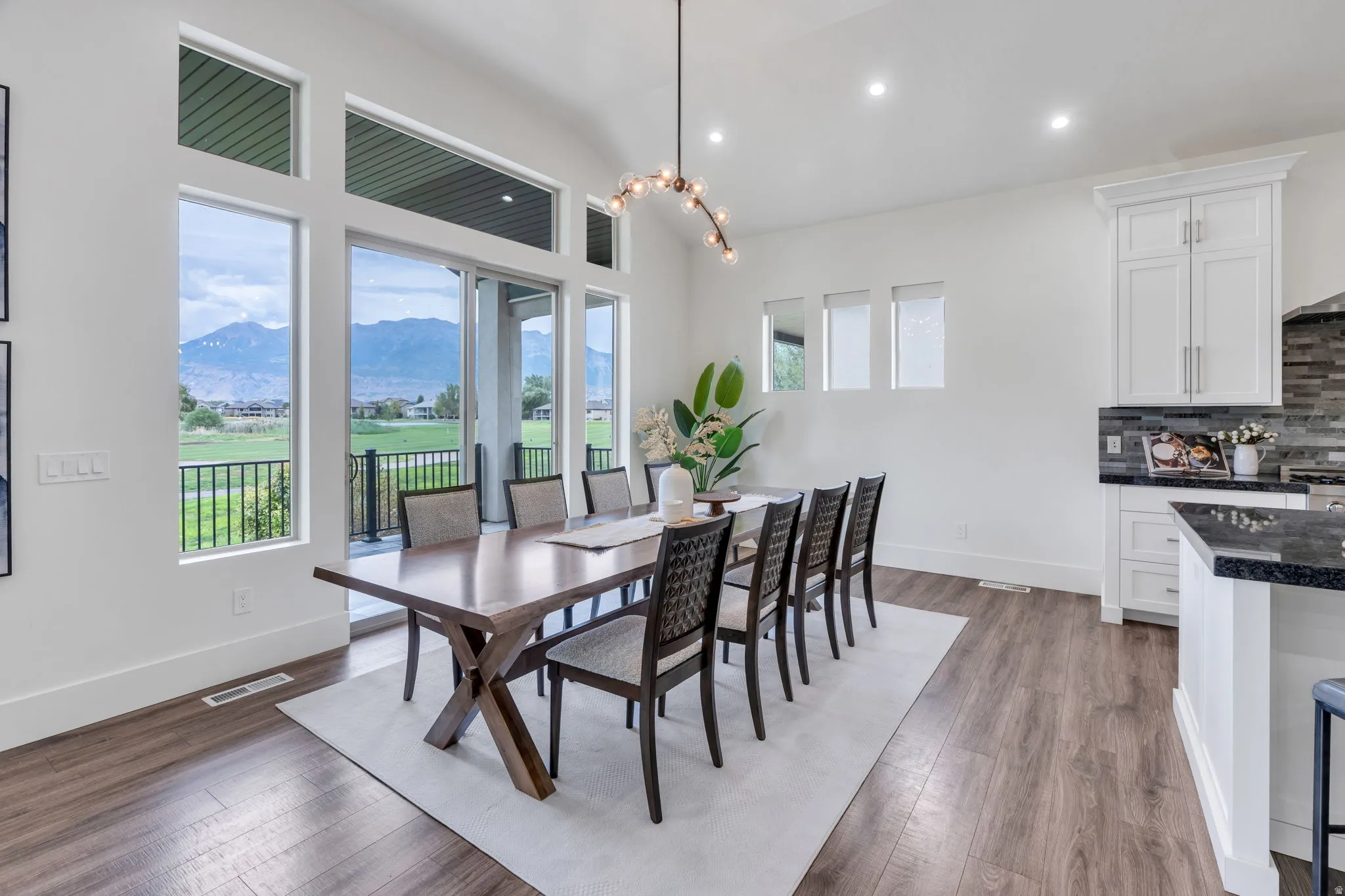 Expansive windows and sliding glass door, vaulted ceiling, wood-finish flooring, recessed lighting, and white cabinetry