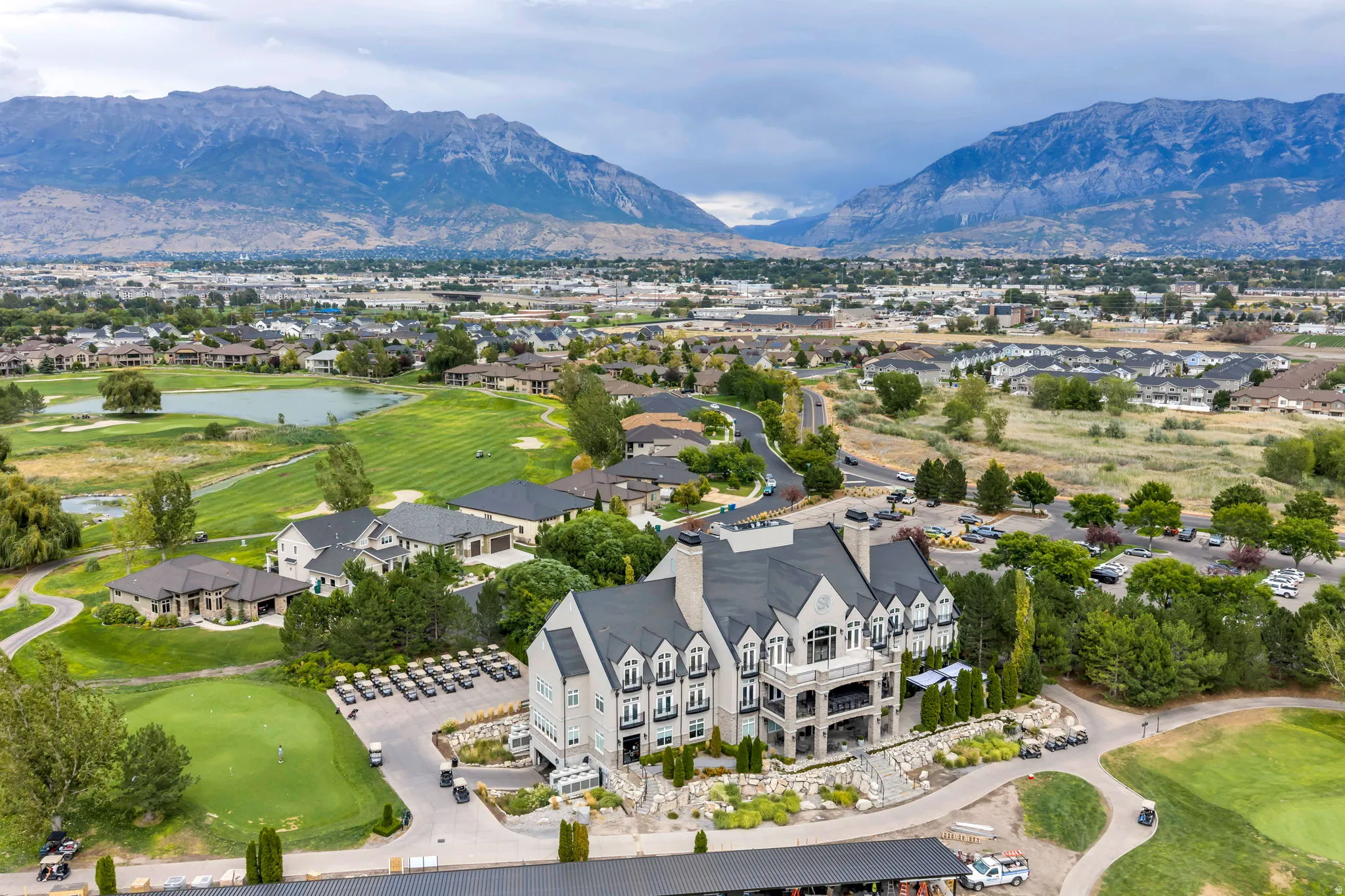 Expansive property featuring a multi-story building with balconies, a golf course, surrounding residential structures, and distant mountains