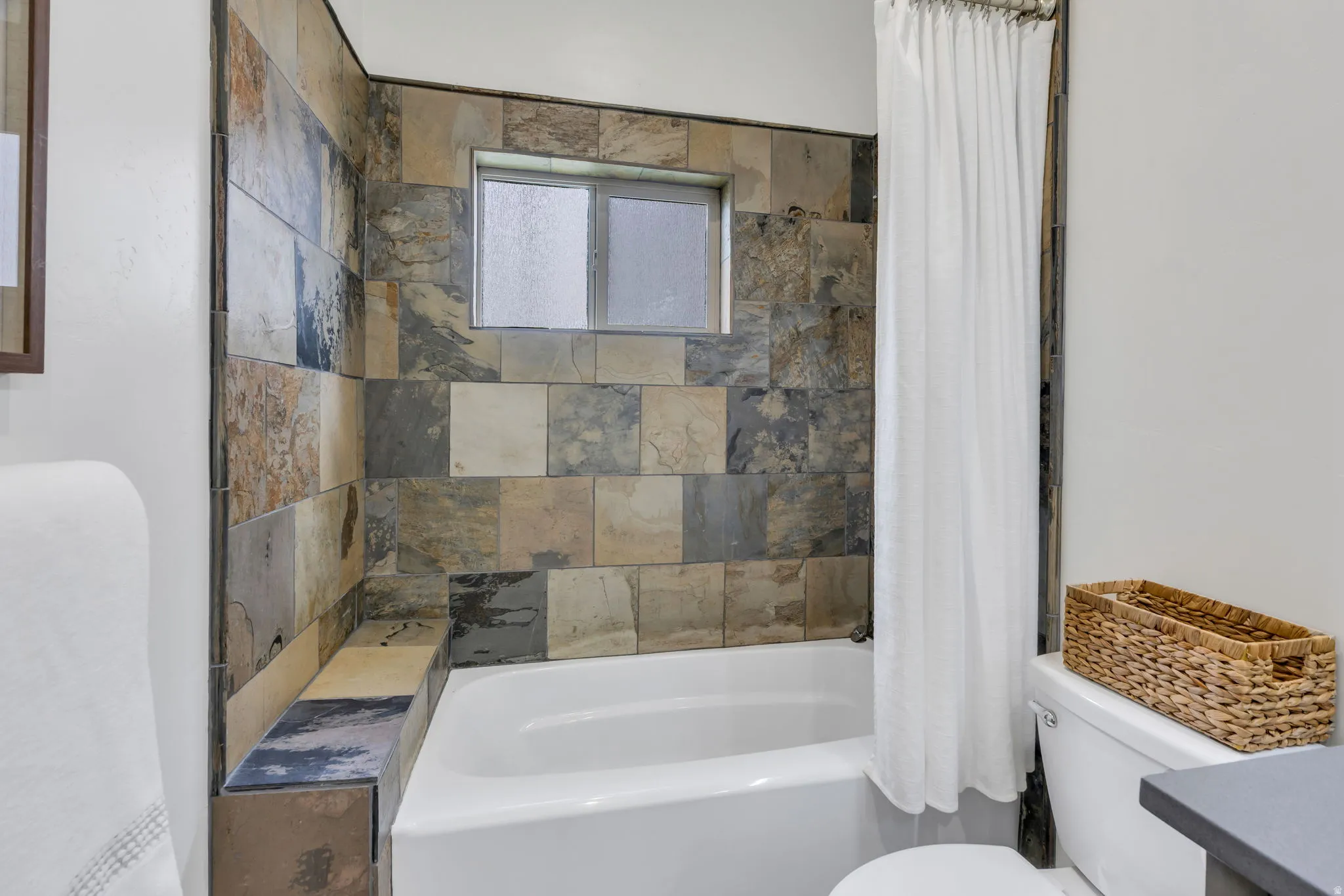 White bathtub with a tiled surround featuring a built-in ledge and a privacy window