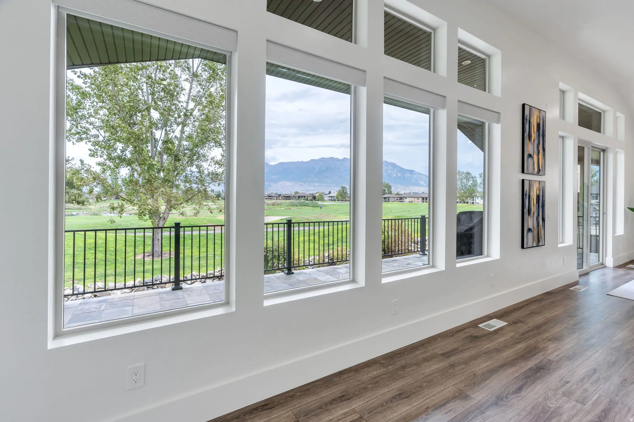Expansive window wall with multiple panes and transoms, wood-finish flooring, white baseboards, and a glass sliding door