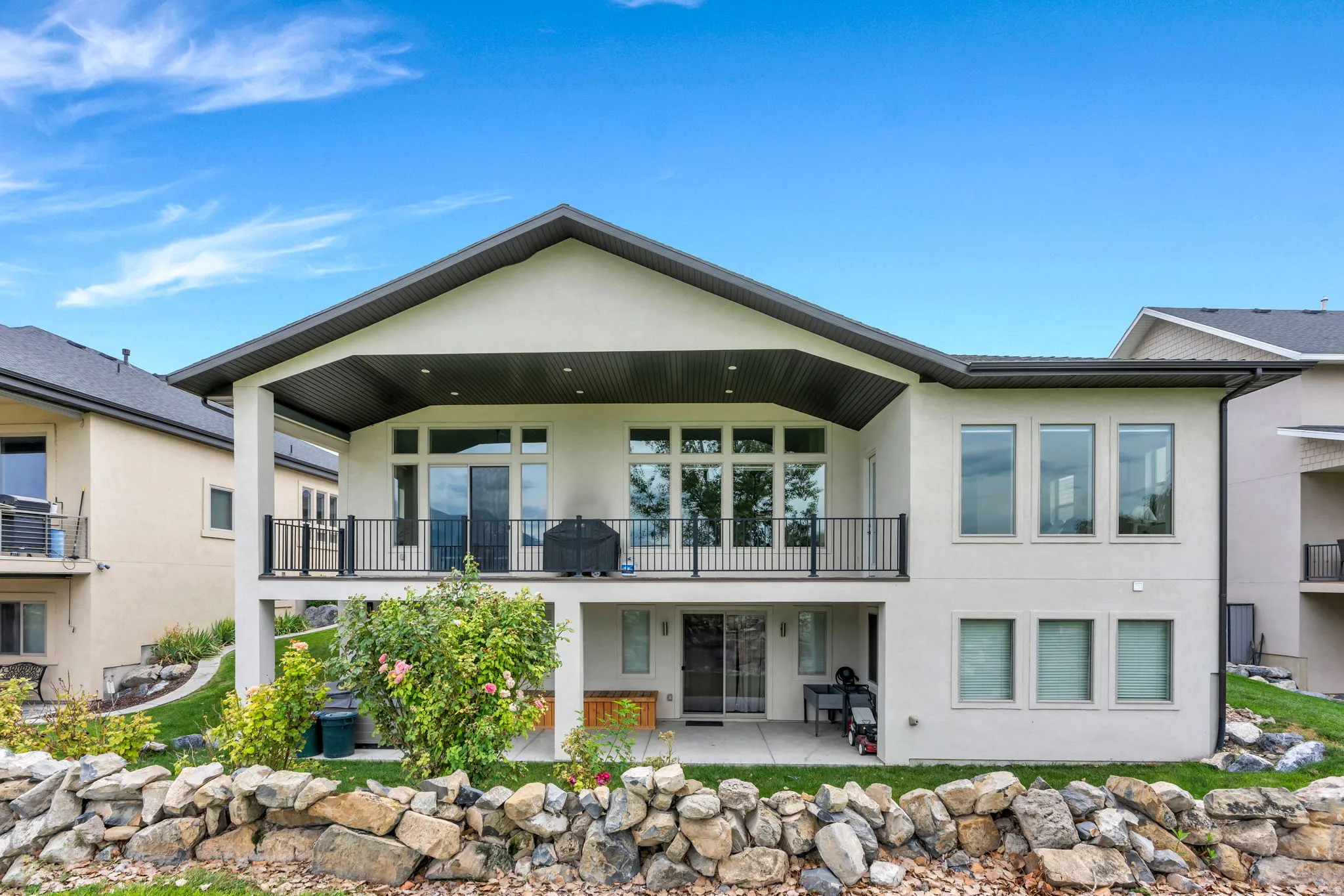 Modern two-story residence featuring a clean-lined gabled roofline, expansive multi-pane windows, and a covered front balcony with glass railings