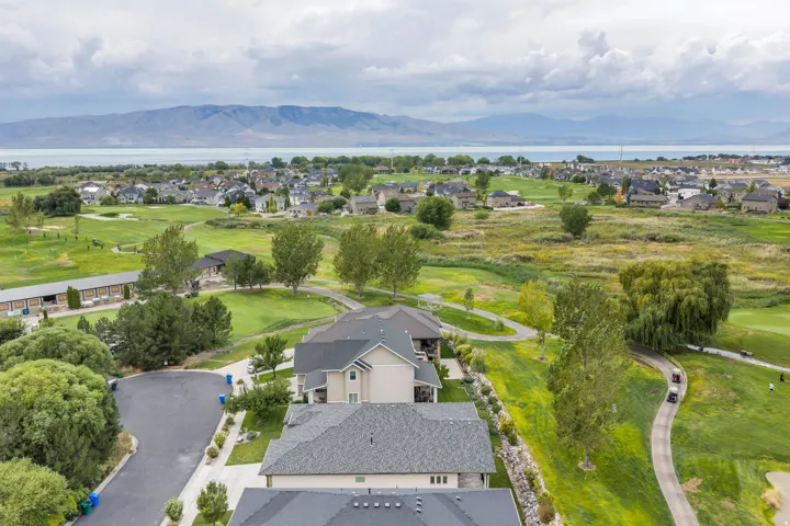 Aerial perspective showcasing residential properties, expansive green spaces, and distant body of water with mountains