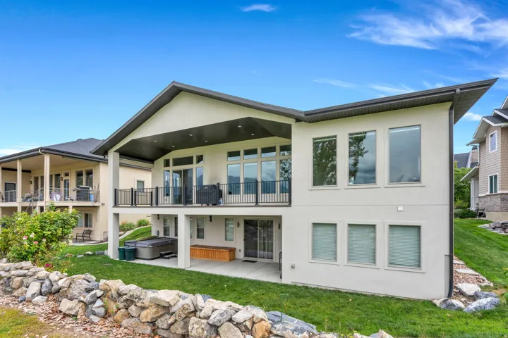 Modern stucco exterior with an angled roofline, upper-level balcony with black railing, lower-level covered patio, and expansive windows