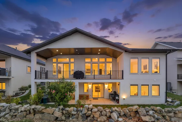 Multi-level property with an upper-level balcony featuring black iron railings, a covered patio on the lower level, and extensive large format windows