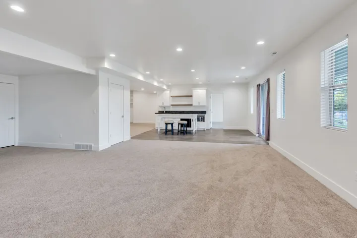 Recessed lighting throughout, two windows with blinds, a sliding glass door, a built-in kitchen area with white cabinetry, and wood-finish flooring