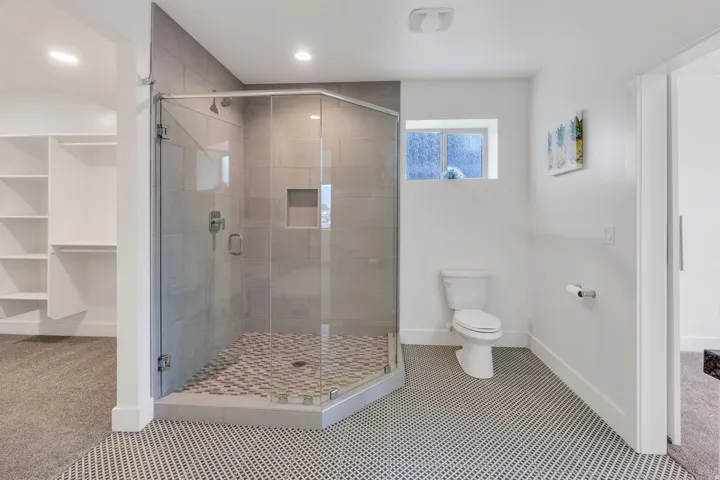 Glass-enclosed shower with tile surround and built-in niche, white toilet, and patterned floor tile