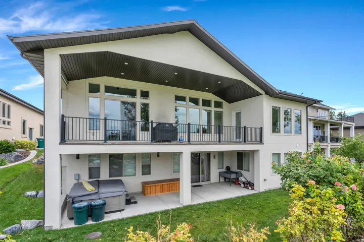 Multi-level stucco exterior with an upper covered balcony featuring black railings, and a lower covered patio