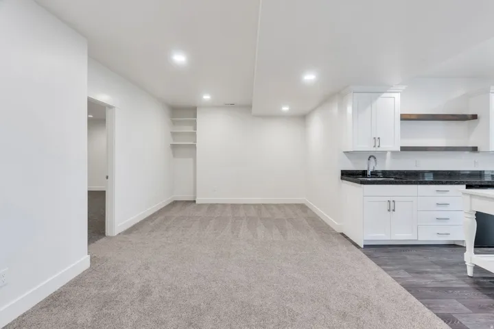 Recessed lighting, built-in shelving, white cabinetry, dark stone countertop, and wood-finish flooring