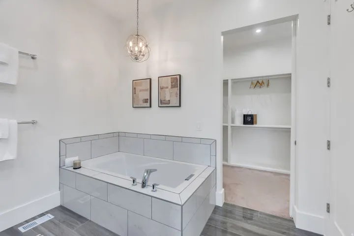 Soaking tub with tile surround, wood-finish flooring, recessed lighting, and an adjacent walk-in closet