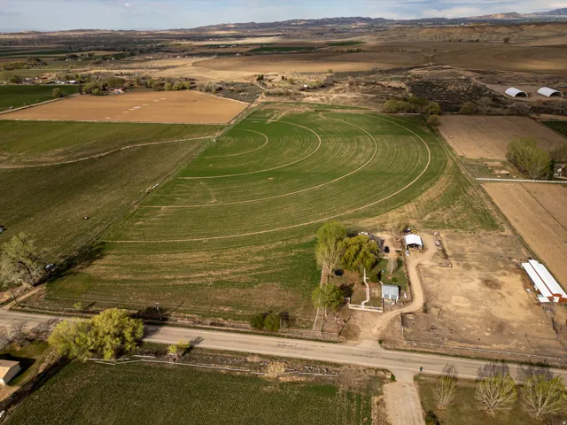 Expansive agricultural property featuring cultivated fields, a residence, auxiliary structures, and surrounding natural terrain
