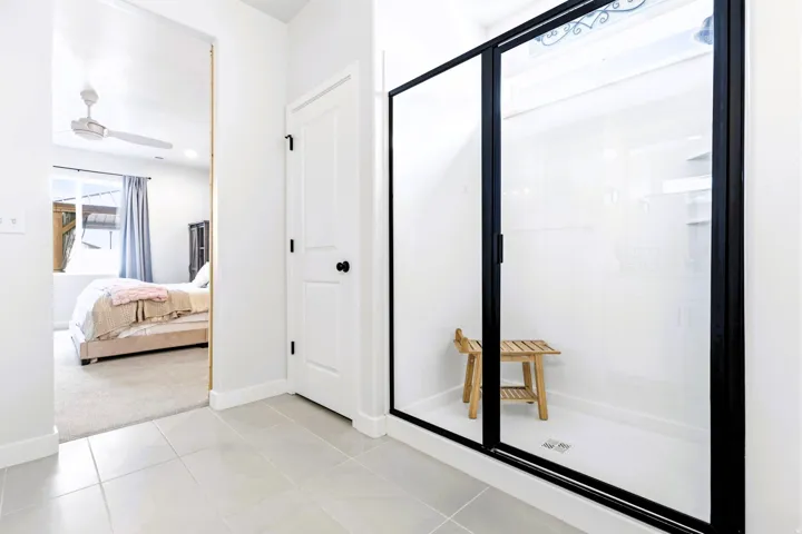 Primary bathroom, walk-in shower with black-framed glass enclosure, white tile flooring, and white interior walls