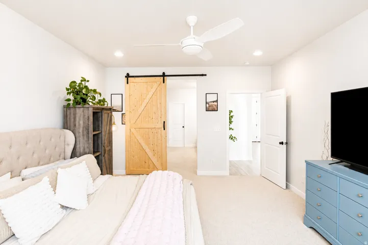 Primary bedroom with recessed lighting, ceiling fan, natural wood barn door, paneled interior door, and light-toned carpeting