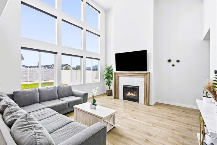Two-story living area with expansive picture frame windows, wood-finish flooring, a contemporary fireplace with a tile surround, and a vaulted ceiling