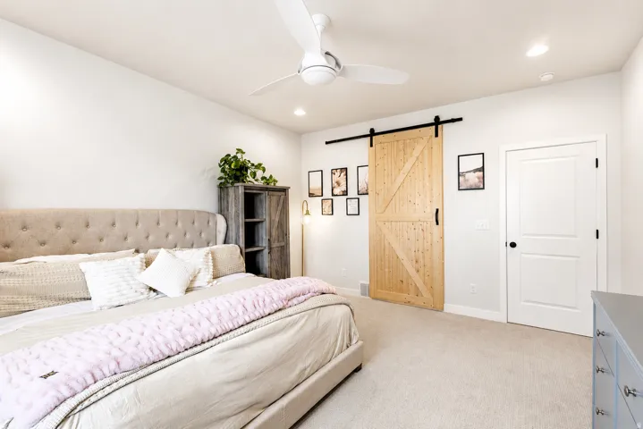 Primary bedroom with recessed lighting, ceiling fan, natural wood-finish barn door, and neutral carpeting