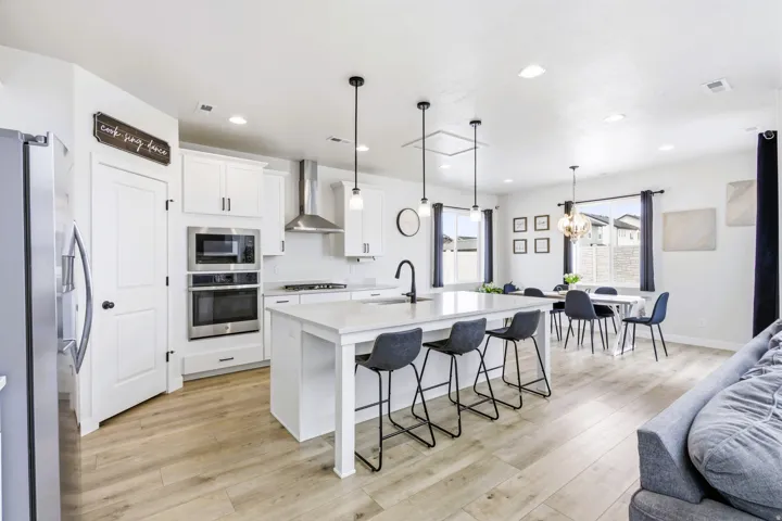 Open-concept kitchen and dining area featuring light wood-finish flooring, white cabinetry, a central island with counter seating, and recessed lighting