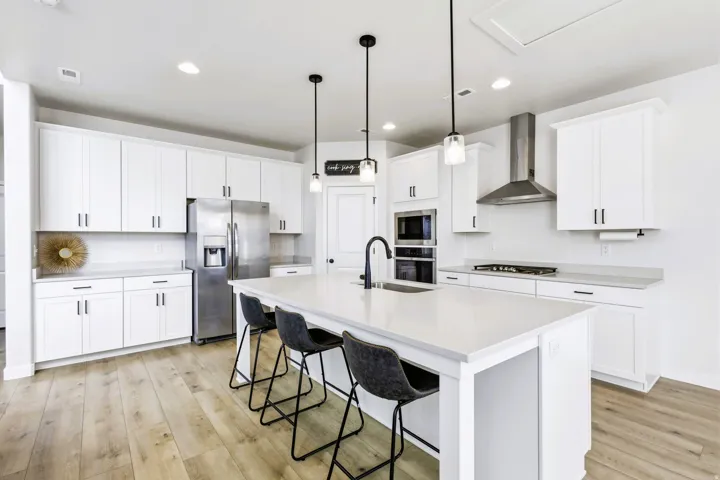 Contemporary kitchen featuring white shaker cabinetry, stainless steel appliances gourmet appliances, a large center quartz island countertop and seating for multiple guests, pendant lighting, and wood-finish flooring throughout the open-concept space