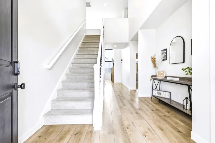 Foyer with light wood-finish flooring, white walls, and a carpeted staircase with white risers and handrail