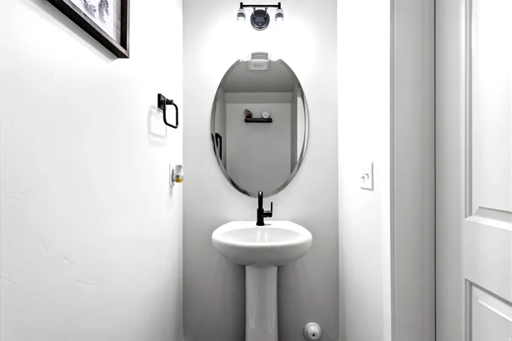 1/2 bath pedestal sink with a matte black faucet, oval mirror, and wall-mounted light fixture