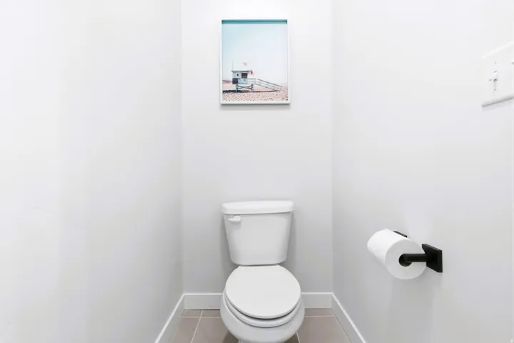 Primary bath, white two-piece toilet with a matching seat, paired with a matte black toilet paper holder and light-toned tile flooring