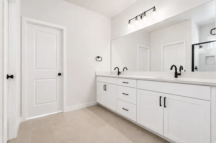 Primary bathroom with dual vanity, quartz countertop, white cabinetry and matte black hardware, under-mount sinks, and a full-width mirror