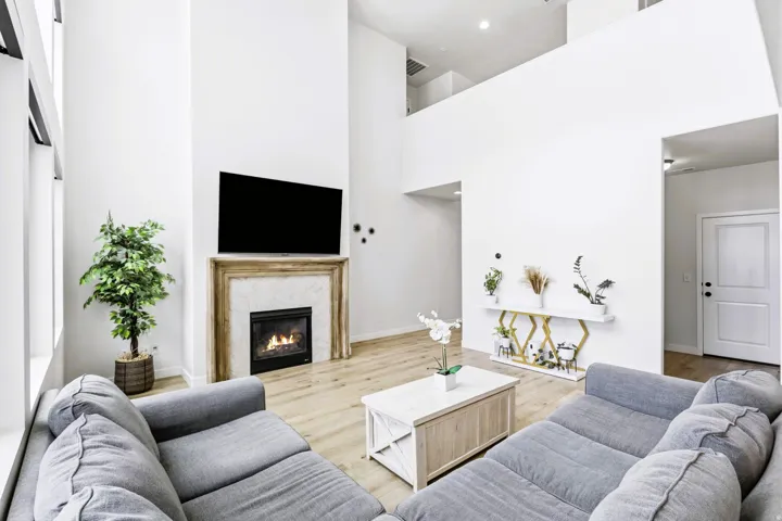 Soaring ceilings, light wood-finish flooring, and an elegant fireplace with a substantial mantel