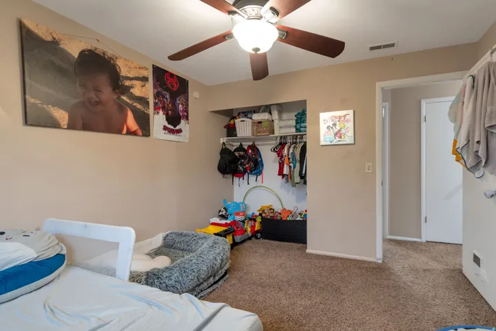 Carpeted room featuring a ceiling fan with integrated lighting, a built-in closet with shelving and hanging rods, and a doorway