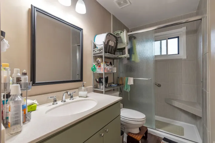 Vanity with integrated sink and chrome faucet, framed mirror, fully tiled shower with built-in bench, and sliding glass shower door