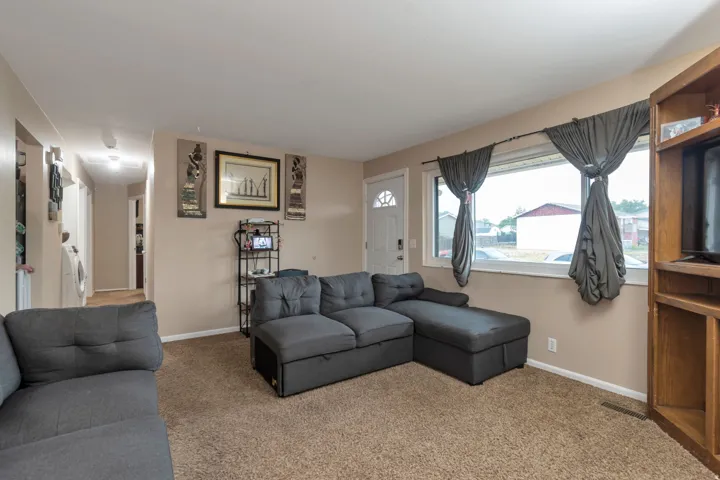 Carpeted living space with a front entry door, a large window, and light-colored walls