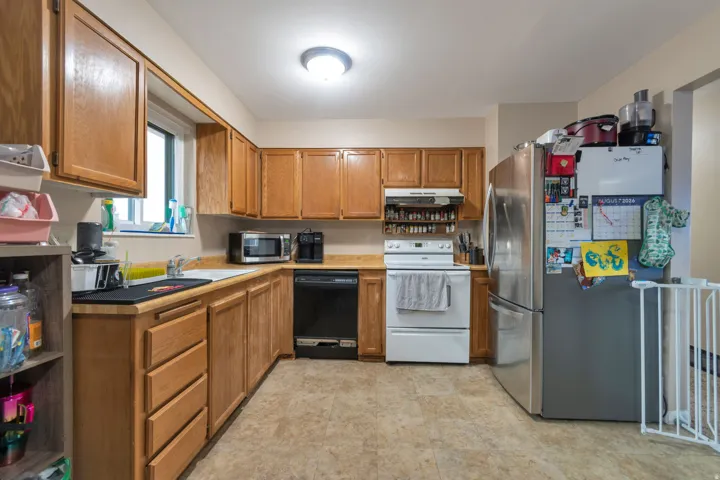 Laminate flooring, wood-finish cabinetry, stainless steel refrigerator, white electric range, and black dishwasher