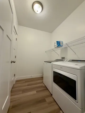 Spacious laundry room with storage shelf, LVP flooring with white baseboards, a flush-mount ceiling light, and a large storage closet