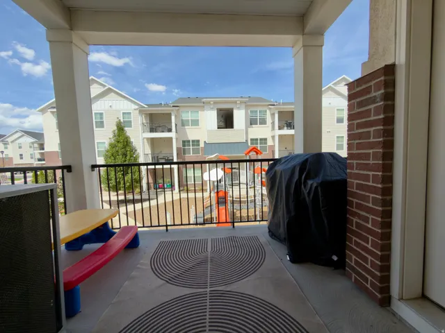 Outdoor covered deck off the family room with black metal railing, and a brick accent column overlooking the playground