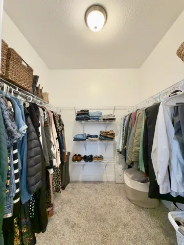 Primary bedrooms large walk-in closet featuring built-in wire shelving and hanging rods