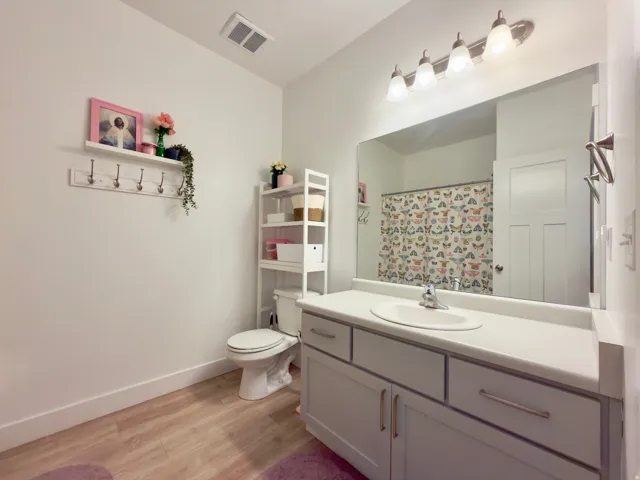 Hall bathroom featuring a single vanity with an integrated sink, grey cabinets, a toilet, a shower/tub combination, and LVP flooring