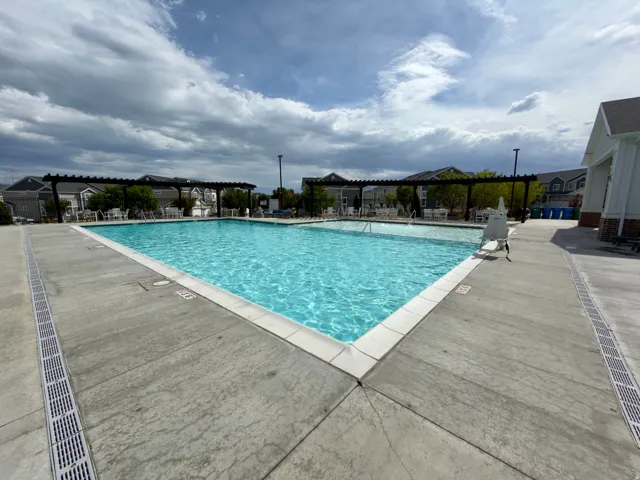 Expansive outdoor swimming pool with surrounding concrete decking, integrated drainage system, and overhead pergolas for shaded seating