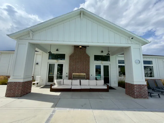 Clubhouse covered outdoor patio area featuring a brick fireplace, board and batten siding, and recessed lighting