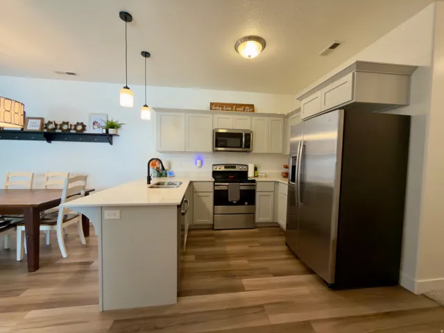 Kitchen featuring LVP flooring, grey cabinetry, stainless steel appliances, and a peninsula with a white quartz countertop