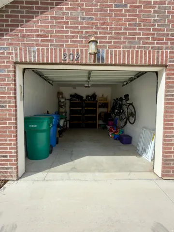 Brick exterior with a garage door, featuring an exterior wall light fixture and house numbers. Lots of storage room inside the garage.