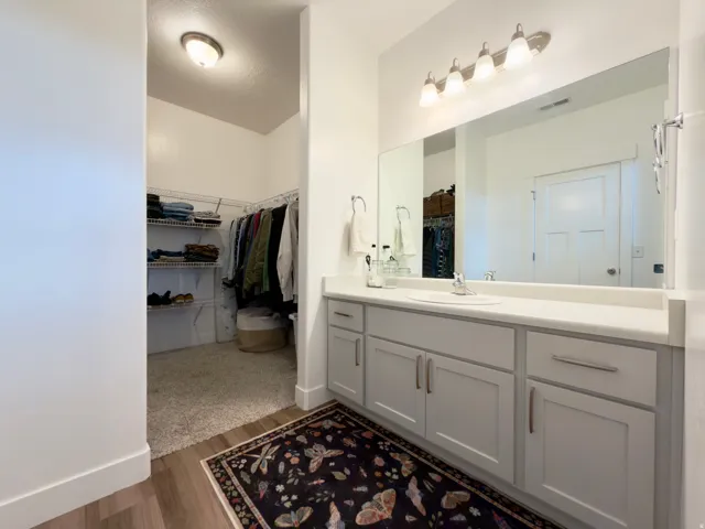 Primary bathrooms light gray vanity with brushed nickel hardware, white countertop, and walk in closet