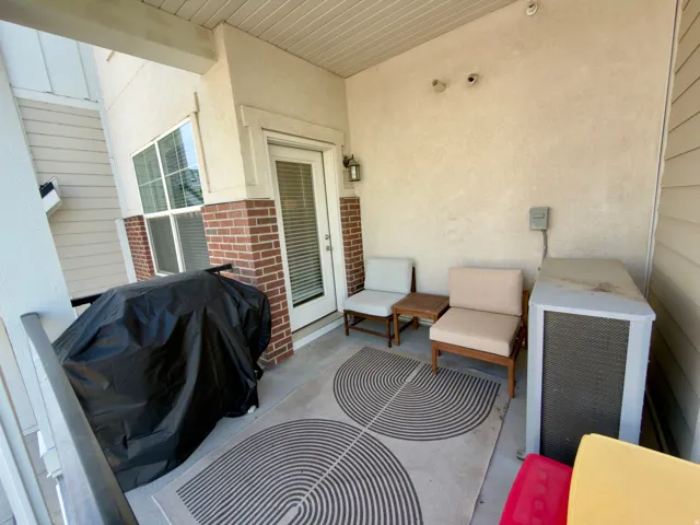 Outdoor covered deck with stucco and brick exterior, white exterior door, and exterior lighting fixture