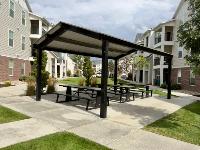 Shaded outdoor common area featuring a metal-framed pergola, integrated picnic tables, and concrete paving