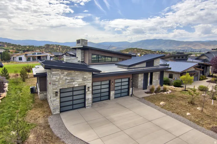 Modern architectural design featuring varied rooflines, stone and wood-look siding, a multi-car garage with frosted glass doors, and a concrete driveway